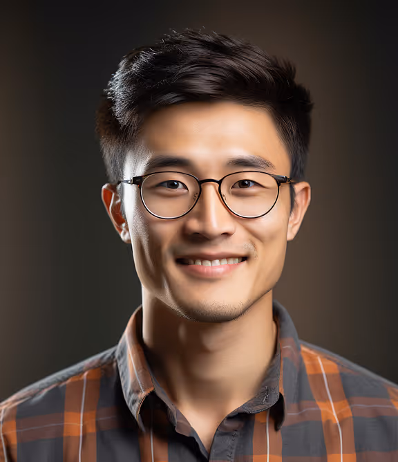 Smiling young man with black-rimmed glasses and dark hair, wearing a brown and gray plaid shirt.